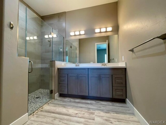 full bath featuring double vanity, a stall shower, a sink, and wood finished floors