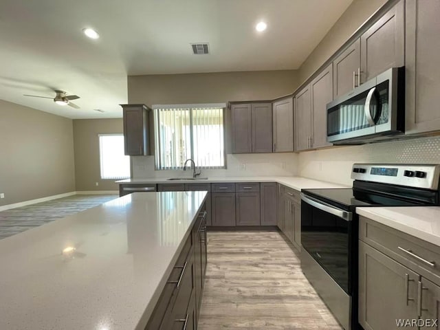 kitchen with stainless steel appliances, a sink, visible vents, light wood-style floors, and decorative backsplash