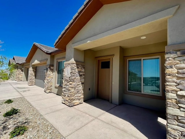 entrance to property featuring stone siding, concrete driveway, an attached garage, and stucco siding