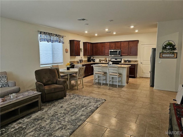 kitchen featuring appliances with stainless steel finishes, open floor plan, light stone countertops, a kitchen island with sink, and a kitchen bar