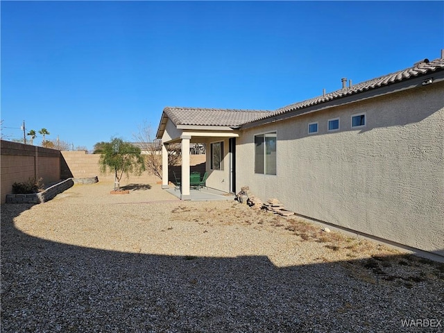 rear view of property with a patio area, a fenced backyard, a tiled roof, and stucco siding