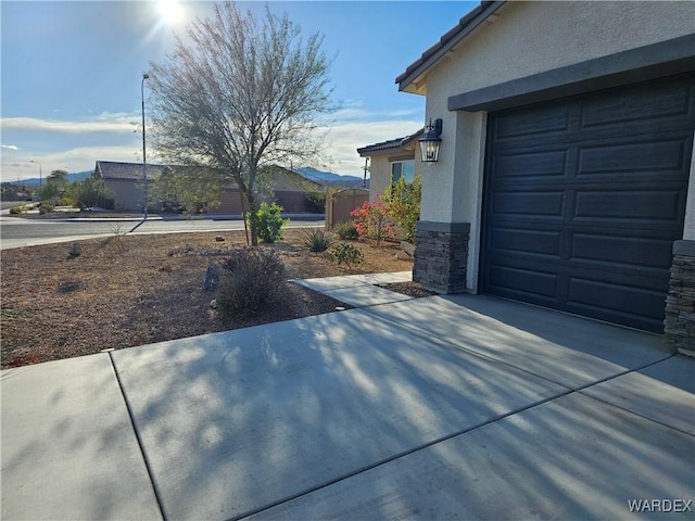 view of home's exterior featuring stone siding, concrete driveway, a tiled roof, and stucco siding