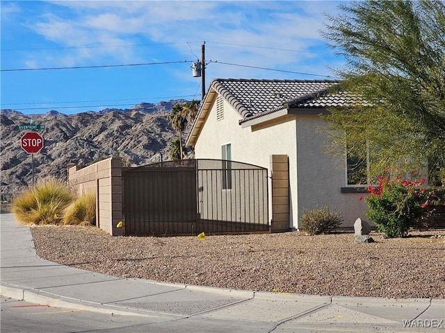 view of home's exterior with a mountain view, fence, a tile roof, a gate, and stucco siding