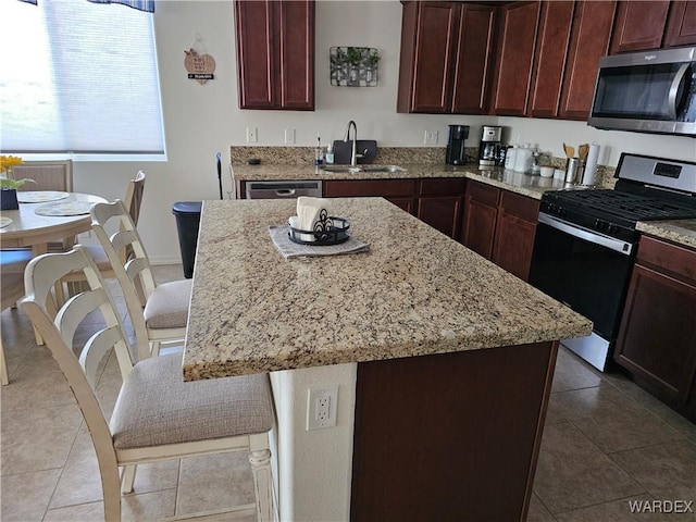 kitchen with stainless steel appliances, a sink, a kitchen island, light stone countertops, and a kitchen bar