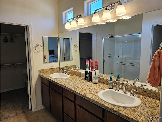 bathroom with double vanity, a stall shower, a walk in closet, and a sink