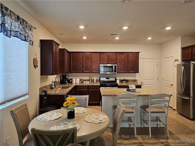 kitchen featuring recessed lighting, a sink, a center island, appliances with stainless steel finishes, and light stone countertops