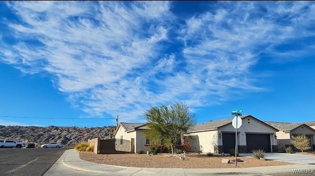 view of front facade with stucco siding, an attached garage, a gate, a mountain view, and driveway