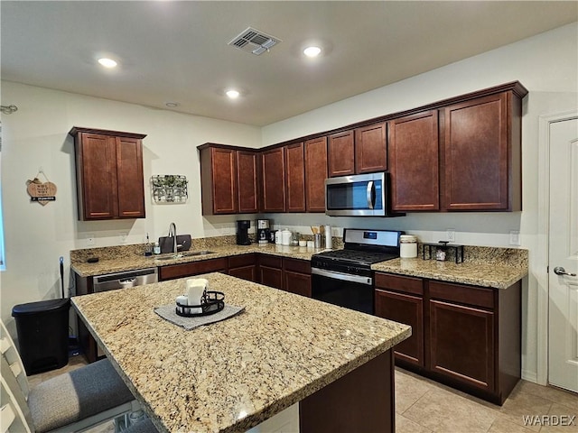 kitchen featuring a center island, a breakfast bar, stainless steel appliances, visible vents, and light stone countertops