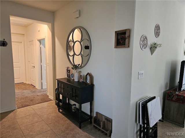 hall featuring carpet floors, tile patterned flooring, and baseboards