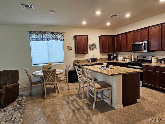 kitchen featuring a center island, a breakfast bar area, stainless steel appliances, visible vents, and light stone countertops