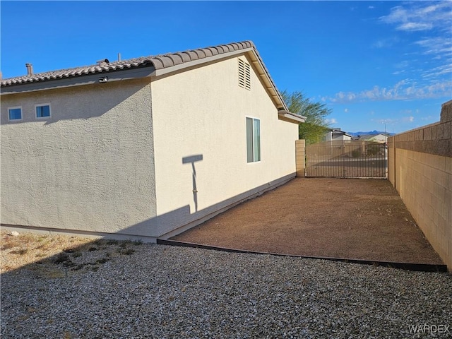 view of property exterior with a gate, a tile roof, fence, and stucco siding