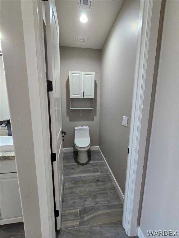 bathroom featuring toilet, wood finished floors, visible vents, and baseboards