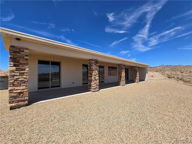 back of property featuring stone siding, a patio, and stucco siding