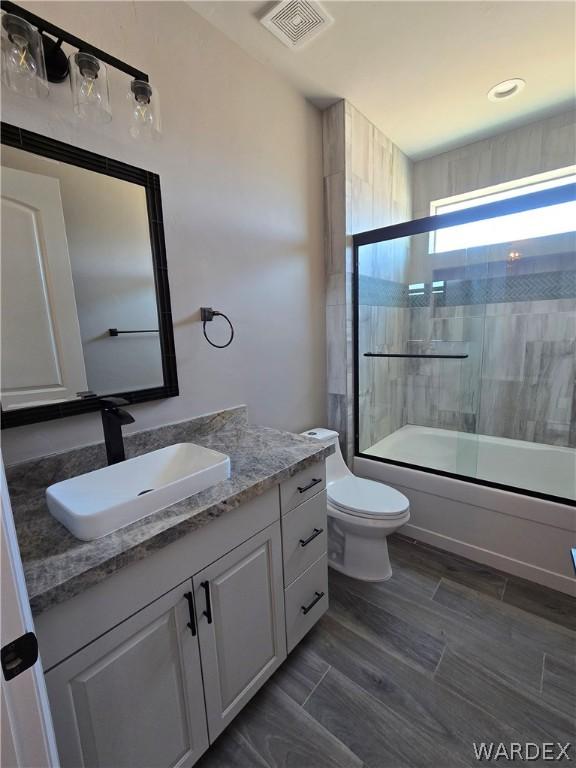 full bath with toilet, bath / shower combo with glass door, wood finish floors, vanity, and visible vents