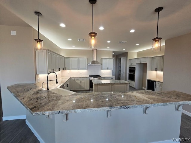 kitchen with stainless steel appliances, wall chimney exhaust hood, a peninsula, and a breakfast bar area