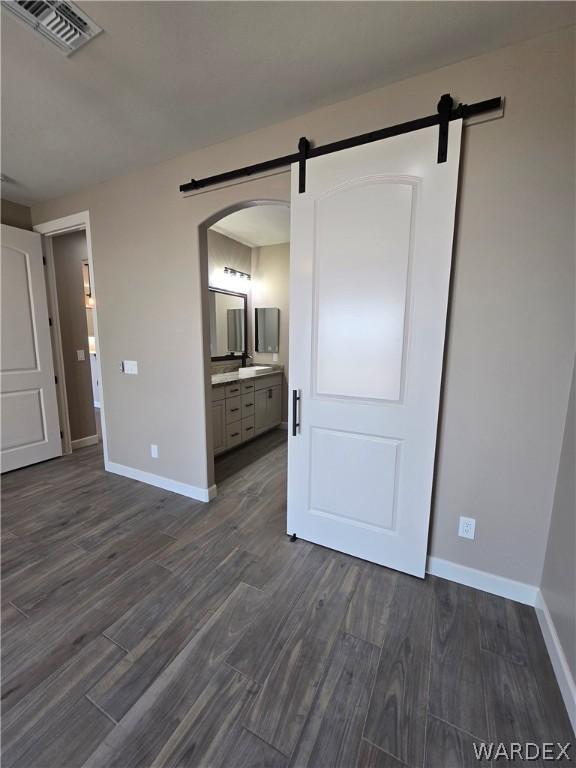 unfurnished bedroom featuring a barn door, dark wood finished floors, and visible vents