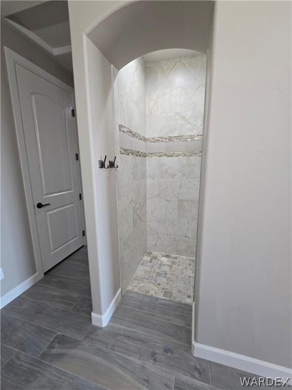 full bathroom featuring baseboards, a tile shower, and wood finish floors