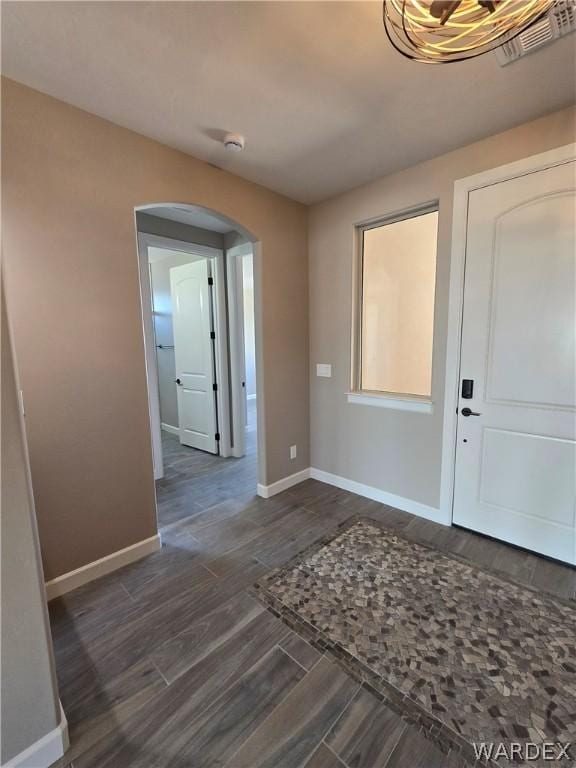 foyer entrance with dark wood-style floors, arched walkways, and baseboards