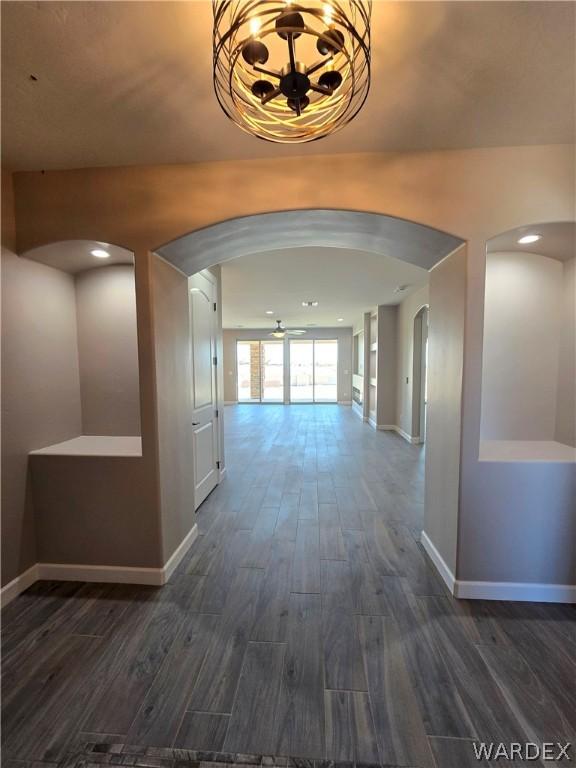 hallway featuring dark wood-style floors, arched walkways, and baseboards