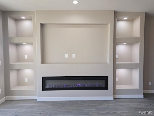 room details with built in shelves, wood tiled floor, a glass covered fireplace, and baseboards