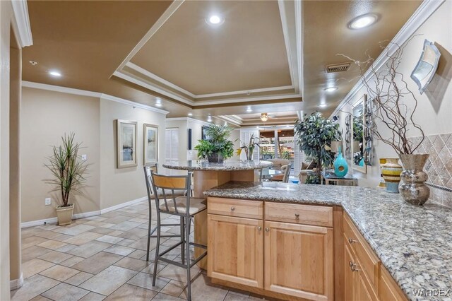 kitchen with visible vents, a kitchen bar, light stone countertops, a raised ceiling, and crown molding