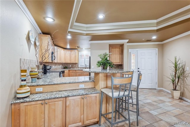 kitchen featuring a peninsula, a tray ceiling, a kitchen breakfast bar, and crown molding