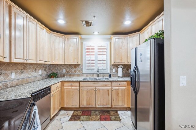 kitchen with light tile patterned floors, appliances with stainless steel finishes, a sink, light stone countertops, and backsplash