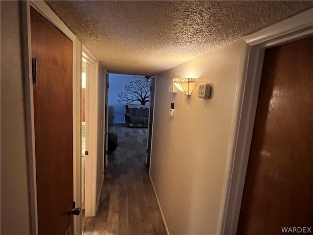 corridor with a textured ceiling, dark wood finished floors, and baseboards