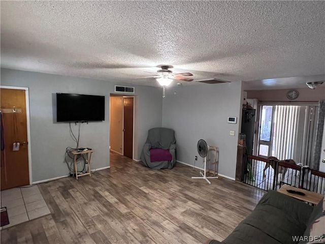 living room with visible vents, a textured ceiling, baseboards, and wood finished floors