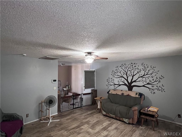 sitting room with ceiling fan, a textured ceiling, baseboards, and wood finished floors