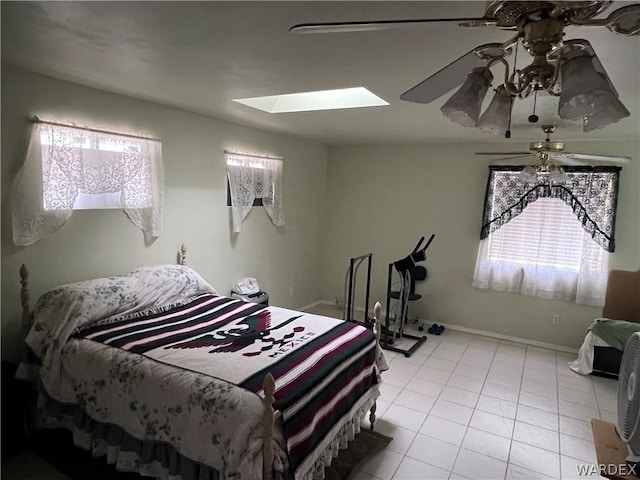 bedroom with light tile patterned floors, ceiling fan, a skylight, and baseboards