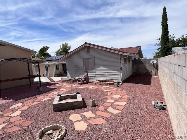 rear view of house featuring a patio, an outdoor fire pit, a fenced backyard, and roof mounted solar panels