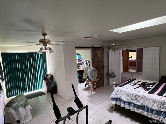 bedroom featuring light tile patterned floors, a barn door, a skylight, visible vents, and ceiling fan