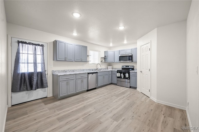 kitchen with light wood-style flooring, gray cabinetry, stainless steel appliances, a sink, and baseboards