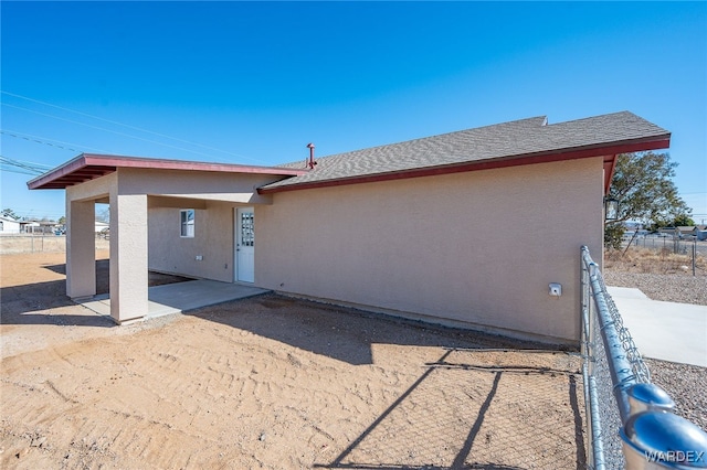 rear view of property with a patio area, roof with shingles, fence, and stucco siding