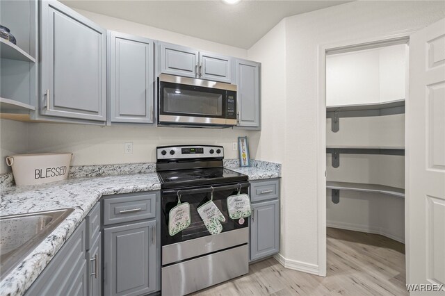 kitchen featuring light wood-style flooring, gray cabinets, stainless steel appliances, open shelves, and a sink