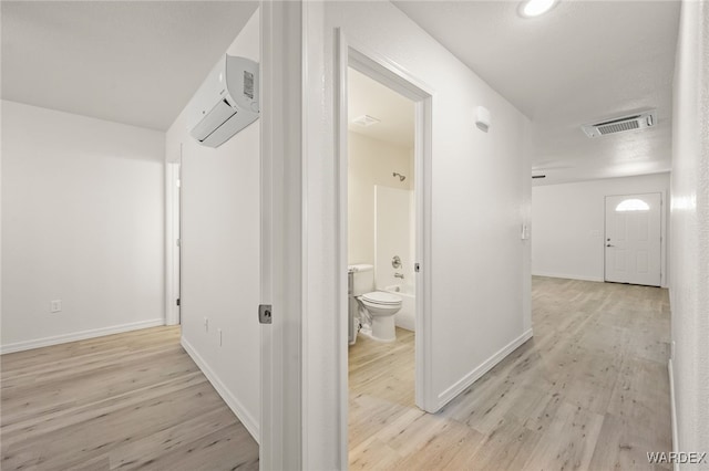 corridor featuring light wood finished floors, a wall mounted air conditioner, visible vents, and baseboards