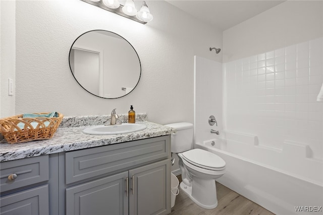 full bath featuring a textured wall, toilet, washtub / shower combination, vanity, and wood finished floors