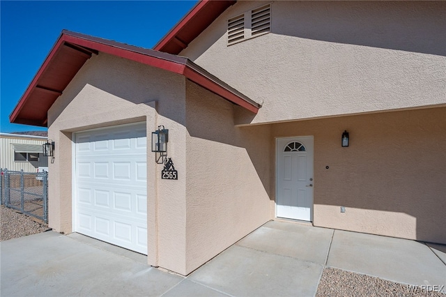 exterior space featuring an attached garage, fence, and stucco siding