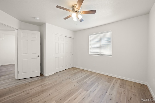 unfurnished bedroom with light wood finished floors, a closet, a ceiling fan, a textured ceiling, and baseboards