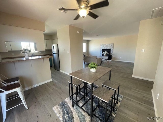 dining space featuring dark wood-style flooring, a fireplace, visible vents, and baseboards