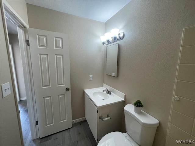 half bathroom featuring a textured wall, vanity, toilet, and wood finished floors