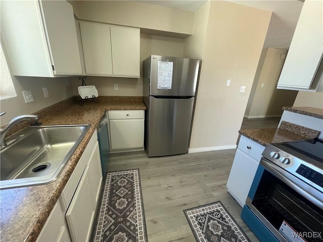 kitchen featuring dark countertops, appliances with stainless steel finishes, light wood-style floors, white cabinetry, and a sink