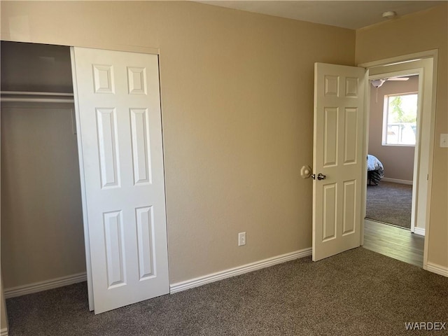 unfurnished bedroom with dark colored carpet, a closet, and baseboards