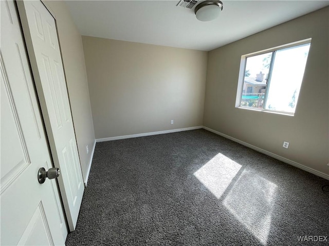 unfurnished room with dark colored carpet, visible vents, and baseboards