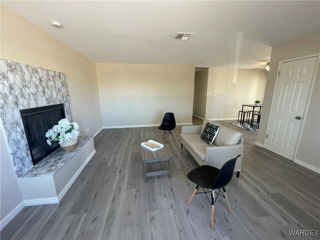 living area with a premium fireplace, wood finished floors, visible vents, and baseboards