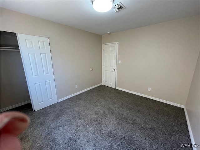 unfurnished bedroom with dark colored carpet, a closet, visible vents, and baseboards