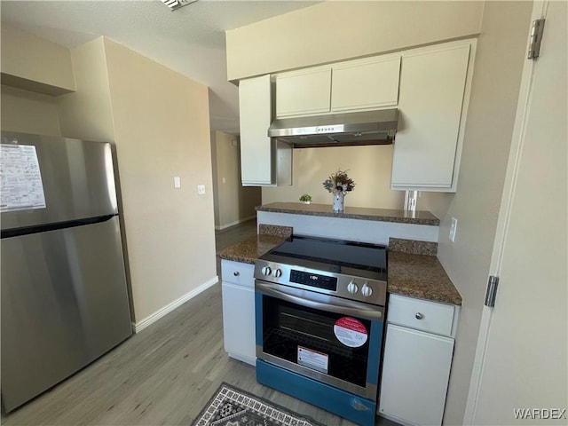 1720 E Valencia Rd, Fort Mohave, AZ 86426 - kitchen with stainless steel appliances, range hood, light wood-type flooring, white cabinets, and dark stone counters