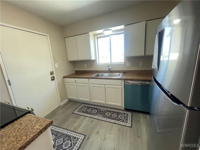 kitchen featuring appliances with stainless steel finishes, dark countertops, a sink, and white cabinetry