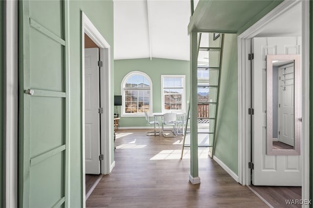 corridor featuring dark wood-type flooring, baseboards, and vaulted ceiling